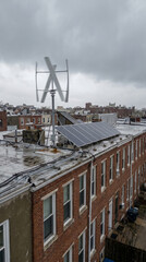 Fototapeta premium Vertical axis wind turbine and solar panels mounted on flat roof of urban brick rowhouse