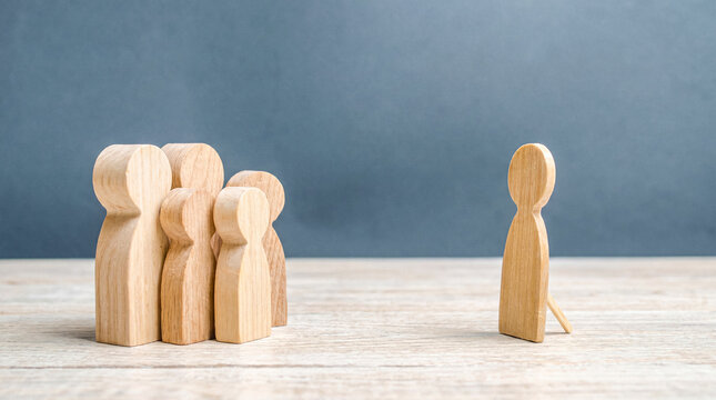 Single wooden human figure facing away from a larger group, representing concepts of solitude, nonconformity.