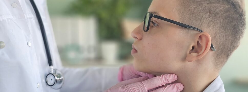 A pediatrician examines the thyroid gland of a little boy in a clinic.