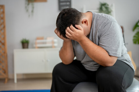 Exhausted Asian plus-size man taking a break while workout in house. 