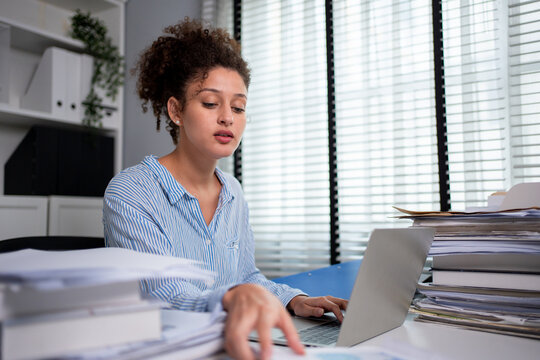 Latina businesswoman working and reviewing documents on desk at office. 