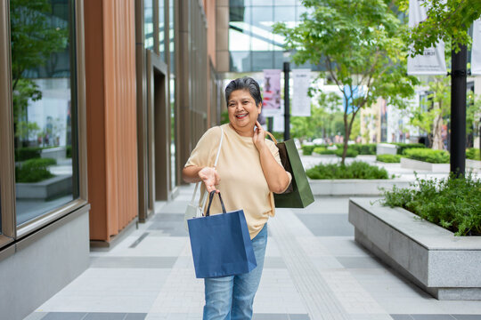 Portrait of Asian senior woman stand outdoors with shopping bags in city