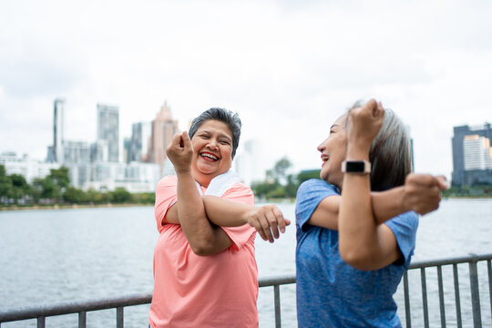 Two Asian senior women stretching body while exercising outdoors in park. 