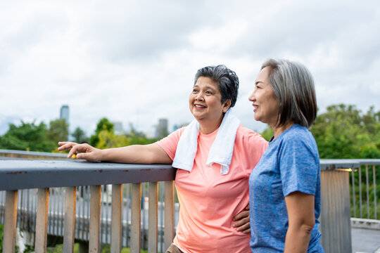 Two Asian senior women taking a break while exercise outdoors in city. 