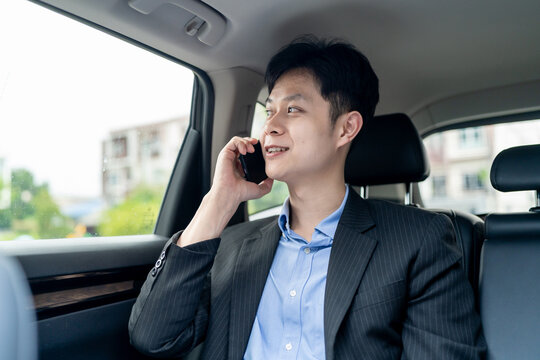 Asian man talking on phone while sitting in the back seat of a car. 