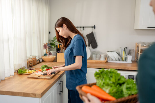 Cheerful young Asian woman preparing fresh vegetables in cozy kitchen. 