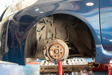 Front car brake disc and wheel hub exposed during maintenance in garage showing automotive repair inspection suspension and safety components on lifted vehicle © JP.Studio
