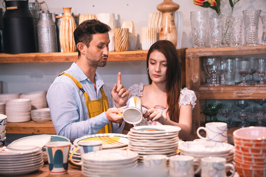Pottery shop assistant and customer select ceramic mug in craft store interior