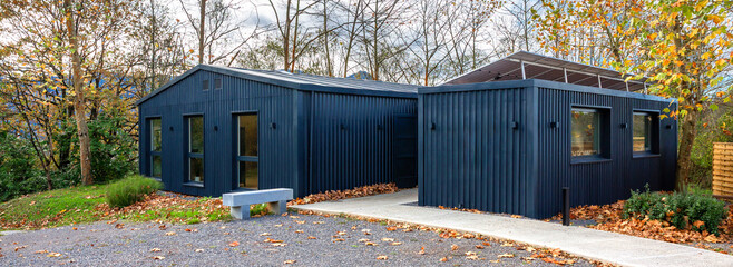 Naklejka premium Banner of modern office building constructed from shipping containers, featuring solar panels, blending contemporary sustainable architecture with the surrounding autumn nature of forest