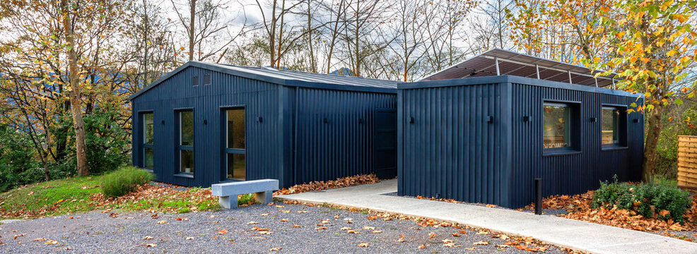 Banner of modern office building constructed from shipping containers, featuring solar panels, blending contemporary sustainable architecture with the surrounding autumn nature of forest