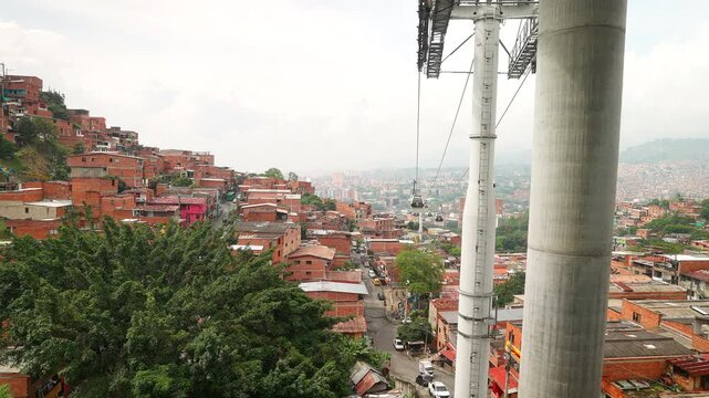 Metrocable car moves over the dense hillside neighborhood of Medellin, Colombia. This public transit system connects urban communities across the valley in South America