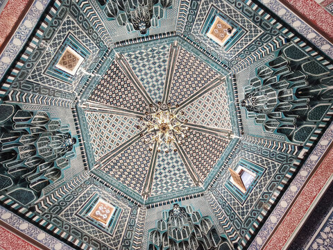 Ornate ceiling with turquoise tilework and chandelier inside Shah-i-Zinda necropolis in Samarkand. Intricate geometric and floral mosaic patterns viewed from below, ideal for travel and cultural.