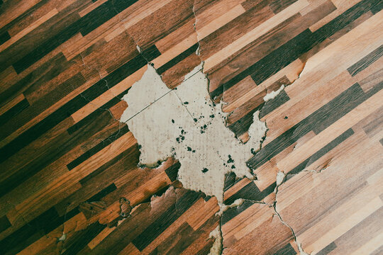 Damaged Wooden Floor with Peeling and Cracked Surface Revealing Concrete Underneath, Water Damage Concept