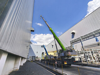 Rear view of boom lift and crane working on factory siding. © WATCHARAPHON