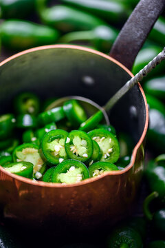 Metal pot with jalapeno slices and spoon inside top view. Fresh green chili cooking preparation with seeds