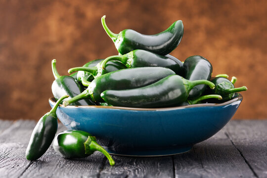 Close view of jalapeno peppers stacked in bowl on wooden table with soft light. Fresh chili, organic produce, food still life, shallow depth