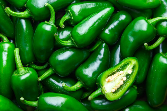 Close view of jalapeno peppers pile with one sliced piece showing seeds. Fresh spicy vegetables texture background