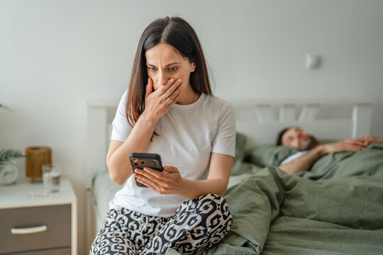 Woman discovering secret text message on smart phone from sleeping partner