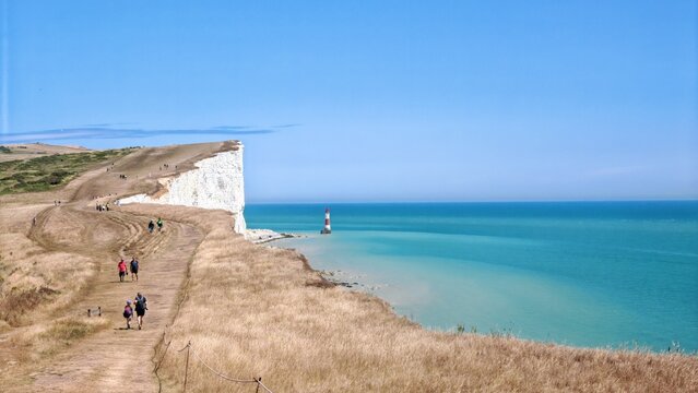 Seven Sisters Cliffs with Beachy Head Lighthouse and hikers, coastal landscape countryside in East Sussex, England UK with travel and adventure concept