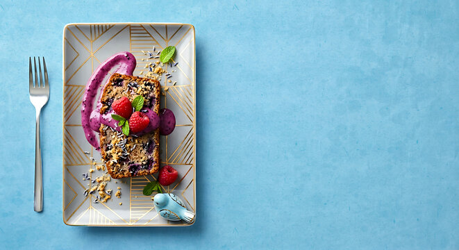 Vegan Blueberry Cake Slice with Berry Sauce and Mint. Flat Lay on Geometric Plate with Decorative Bird Figurine.