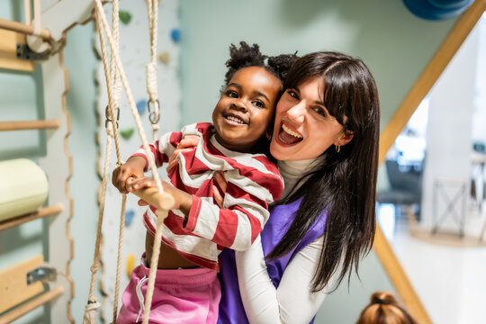 Happy teacher supporting african american child playing on ropes