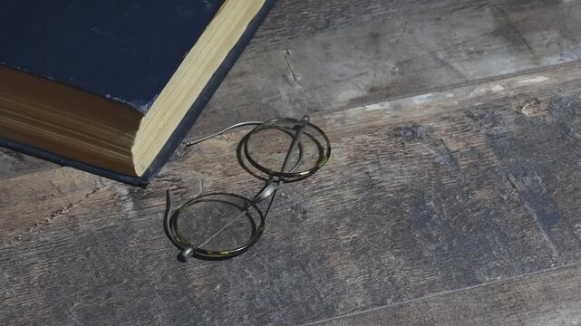 A book and glasses from the past on a wooden table. Retro concept