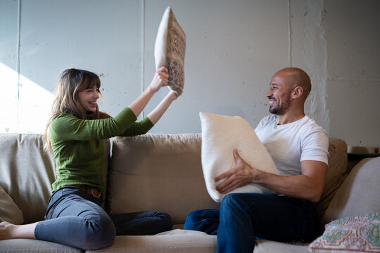 Playful couple laughing during a pillow fight on sofa at home