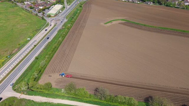Top down aerial drone view of a tractor tilling and ploughing furrows into rural brown fields in the United Kingdom