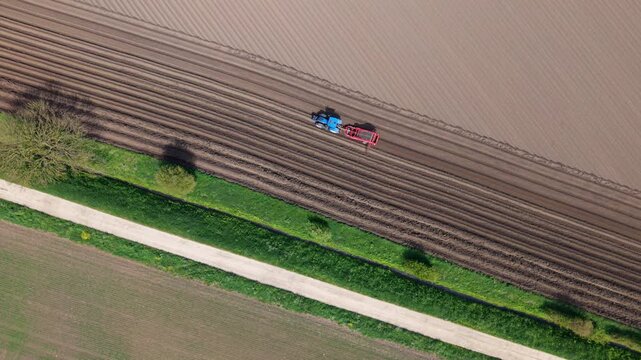 Aerial top down view of a tractor ploughing fields and creating geometric soil furrows near Ferrybridge Yorkshire UK