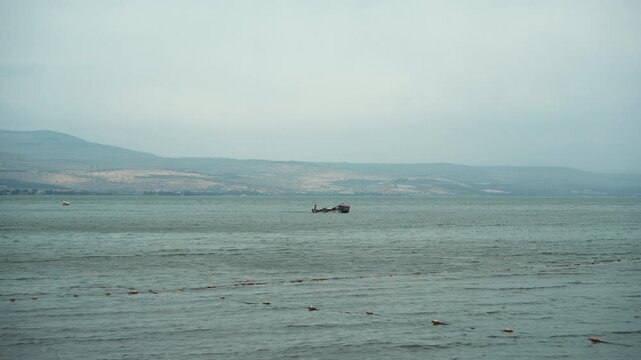 Horizontal Wide-Angle View of a Small Fishing Boat on a Calm Lake under a Hazy Sky with Rolling Hills in the Distance