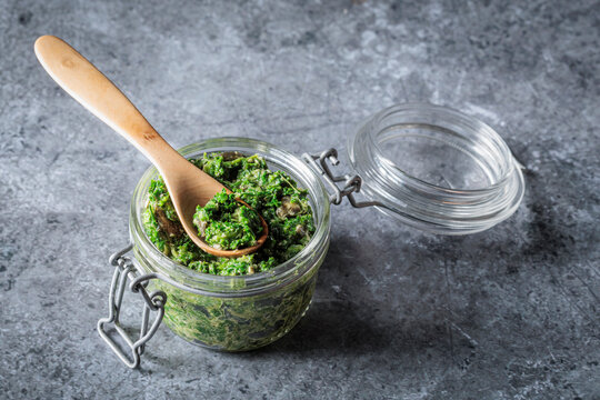 Homemade green pesto in a glass jar with a wooden spoon