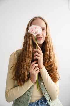 Teenager with blonde hair holding pink flower over eye indoors