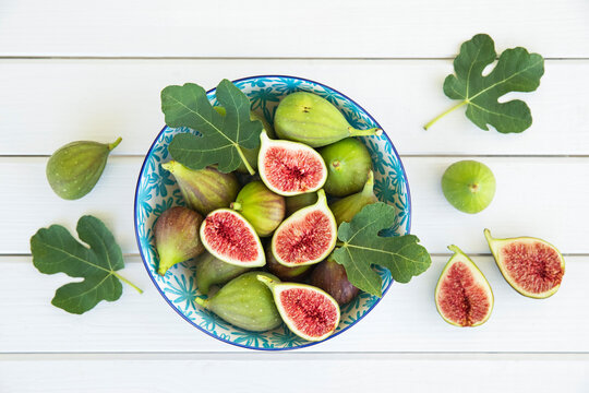 Fresh sliced and whole figs in a bowl on a white table