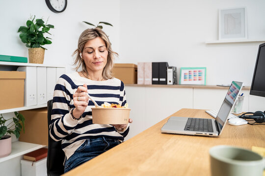 Woman eating salad at her desk in an office with a laptop