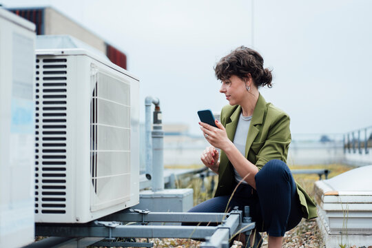 Businesswoman holding smart phone examining HVAC system