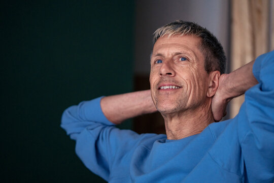 Relaxed senior man with hands behind head sitting at home