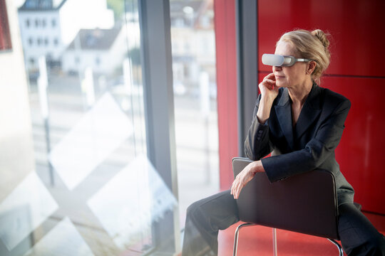 Elderly businesswoman wearing virtual reality headset and sitting on chair