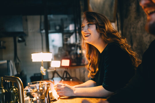 Friends laughing and socializing at a bar counter in evening light