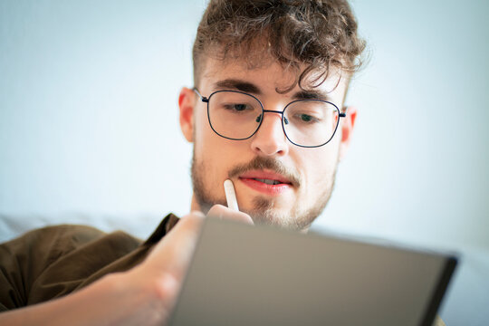 Handsome young man wearing eyeglasses using tablet PC at home
