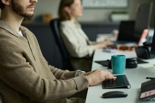 Programmer typing on keyboard at office desk with coworker