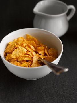 Bowl of dry cornflake cereal with spoon on dark table indoors