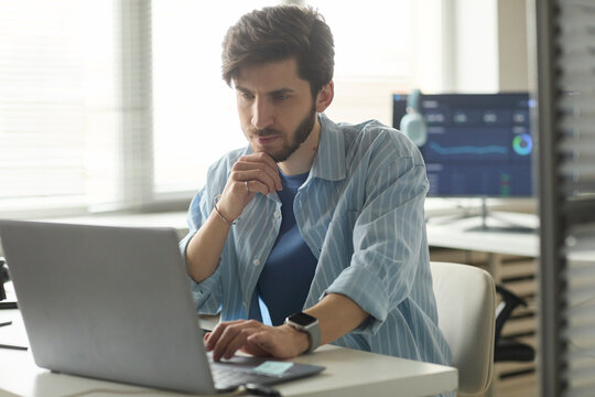 Focused programmer analyzing code on laptop computer in office