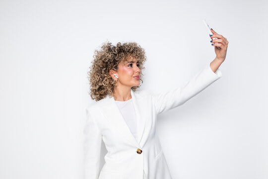 Business woman in a white blazer taking a selfie in a studio with a white background