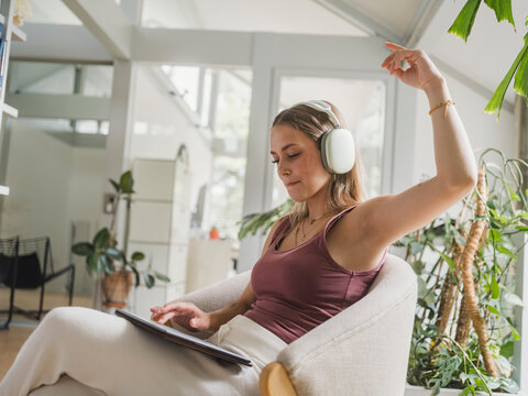 Woman enjoying music with headphones and tablet at home in a soft chair