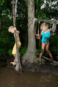 Brother and sister playing outside in mud on a rope swing