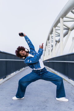 Woman dancing in denim with smartphone on urban bridge