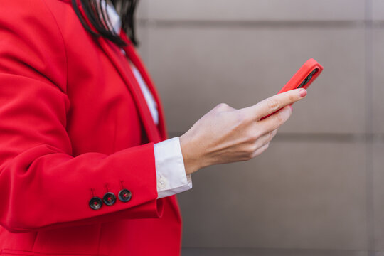 Close up of hand in business attire texting on a red smartphone