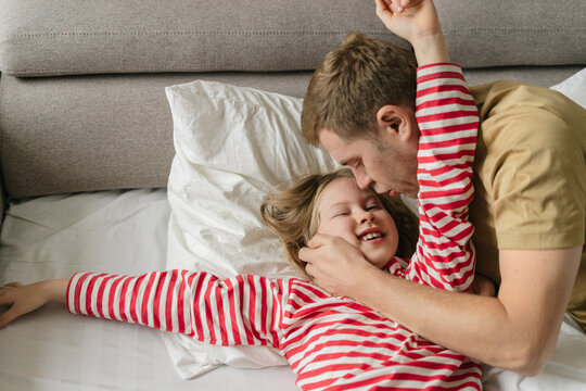 Man waking up daughter lying down on bed at home