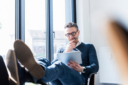 Smiling manager relaxing with tablet at desk in modern office