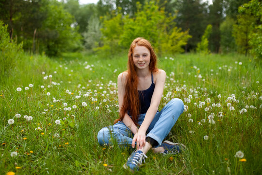 Redhead sitting in a green meadow with dandelions smiling